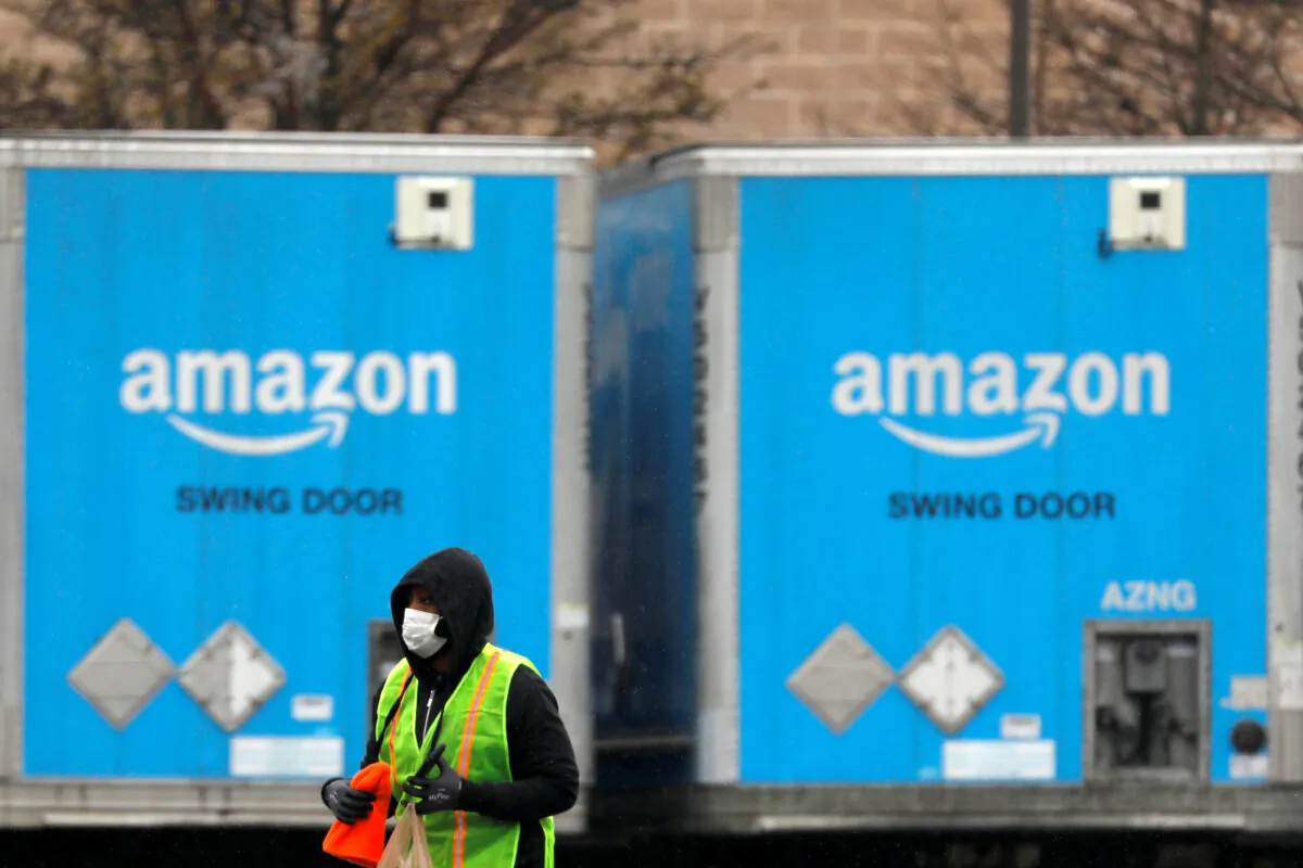 A worker in a face mask walks by trucks parked at an Amazon facility as the global CCP virus (COVID-19) outbreak continued in Bethpage on Long Island in New York, on March 17, 2020. (Andrew Kelly/File Photo/Reuters)