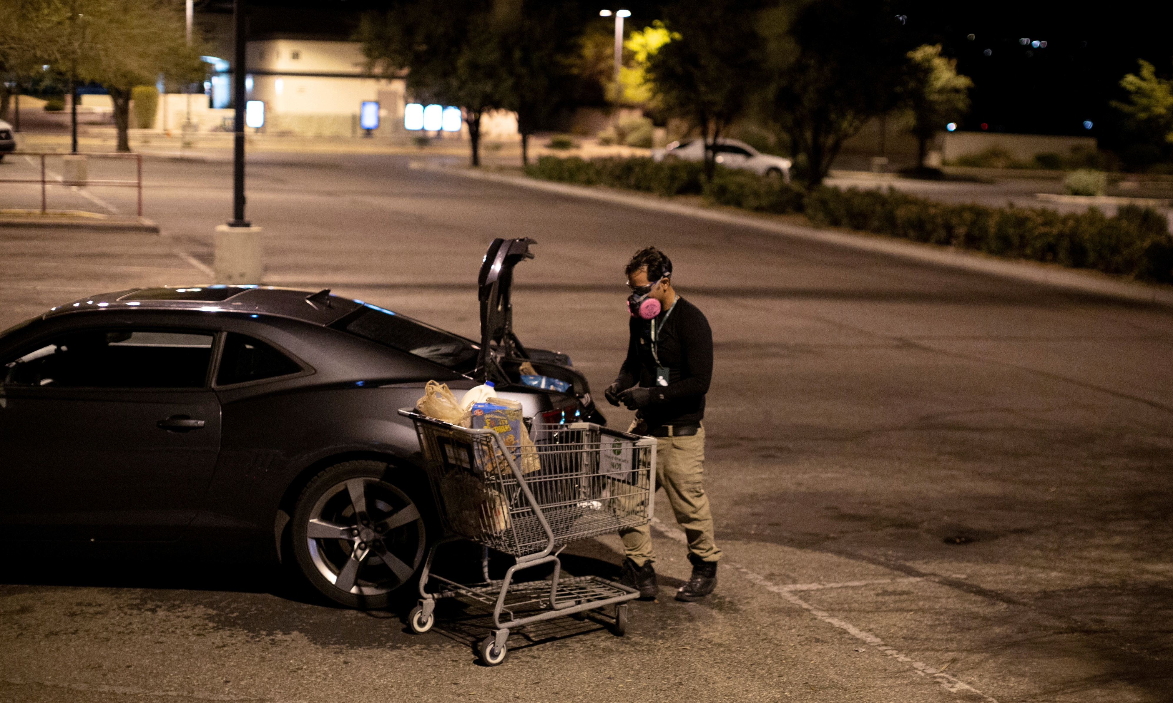 Instacart employee Eric Cohn, 34, loads an order into his car outside a Fry's grocery store while wearing a respirator mask.