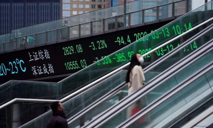 Pedestrians wearing face masks ride an escalator near an overpass with an electronic board showing the Shanghai and Shenzhen stock indexes, following an outbreak of the novel coronavirus in the country, at Lujiazui financial district, in Shanghai, China, on March 13, 2020. (Aly Song/Reuters)