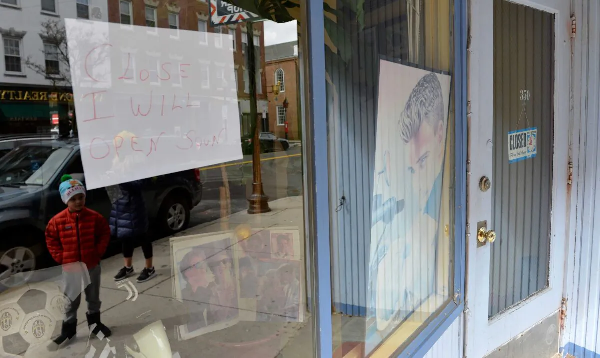 A boy is reflected as he looks into the window of a closed barbershop in Boston, Mass., on March 24, 2020. (Joseph Prezioso/AFP via Getty Images)