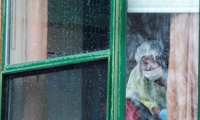 A person wearing protective equipment looks out of a window at the Herron seniors residence on April 13, 2020 in Dorval near Montreal's Trudeau airport. Thirty-one residents are confirmed to have died in the past month. (The Canadian Press/Ryan Remiorz)