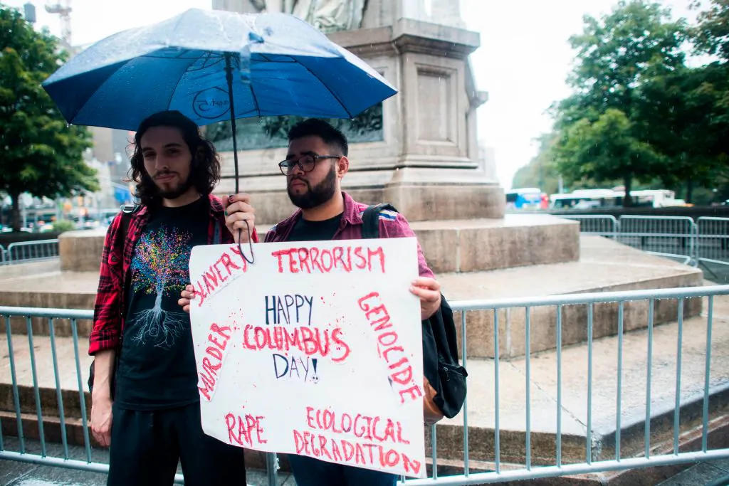 Two protesters display a placard under the statue of Christopher Columbus at Columbus Circle in New York on Oct. 9, 2017, calling for the removal of the statue. (JEWEL SAMAD/AFP via Getty Images)