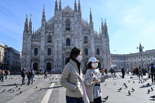 Two women wearing a protective facemask walk across the Piazza del Duomo, in front of the Duomo,