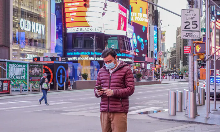 A man wearing a medical face mask is using his phone at Times Square, New York, on April 4, 2020. (Chung I Ho/The Epoch Times)