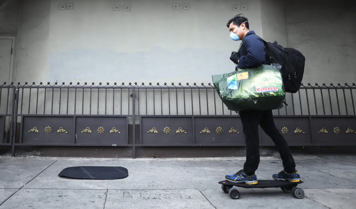 A man skates on the sidewalk while wearing a face mask and carrying bags in Los Angeles, Calif., on March 20, 2020. (Mario Tama/Getty Images)
