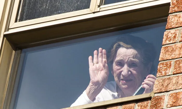 A resident waves as she speaks to her son outside on the sidewalk at the Residence Floralies Lasalle in Montreal on April 15, 2020. Eighteen residents at the facility have died in the last three weeks. (The Canadian Press/Ryan Remiorz)