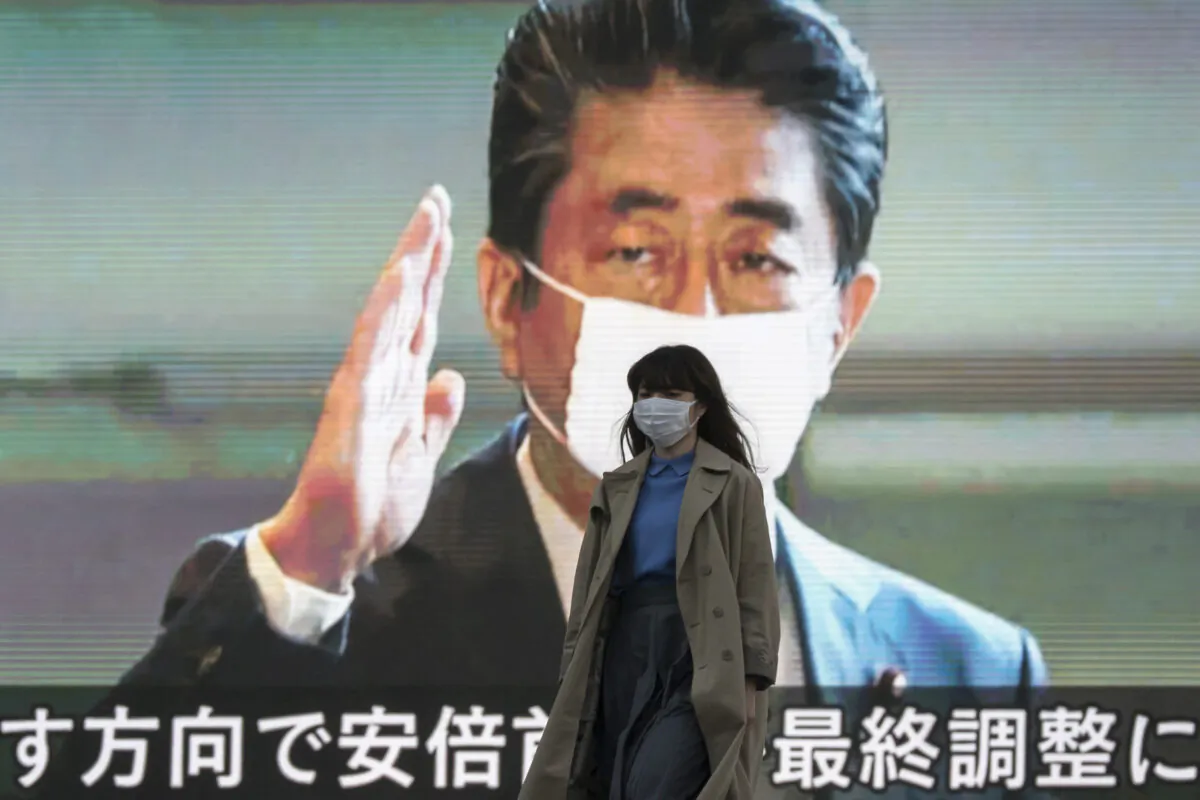 A pedestrian wearing a face mask walks in front of a monitor displaying an image of Japan’s Prime Minister Shinzo Abe during a news broadcast  in Tokyo, Japan, on April 06, 2020. (Tomohiro Ohsumi/Getty Images)