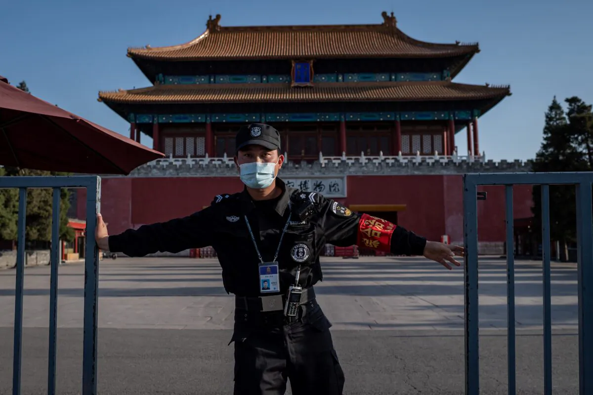 A security guard wearing a facemask amid the concerns over the COVID-19 coronavirus closes a gate outside the forbidden city (back) in Beijing on April 12, 2020. (Nicolas Asfouri/AFP via Getty Images)