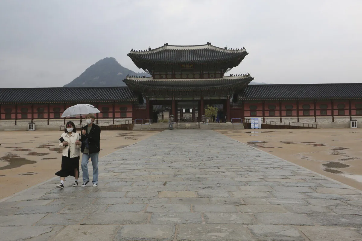 A couple wearing face masks to help protect against the spread of the CCP virus walks in the rain at the Gyeongbok Palace, the main royal palace during the Joseon Dynasty, in Seoul, South Korea, April 17, 2020. (Ahn Young-joon/AP Photo)