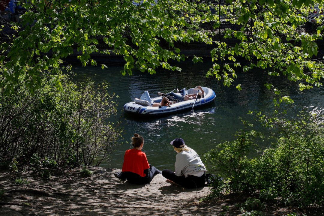 People sit in the sun as others relax in an inflatable boat along the Landwehr canal in Berlin's Kreuzberg district on April 18, 2020. (David Gannon/AFP via Getty Images)