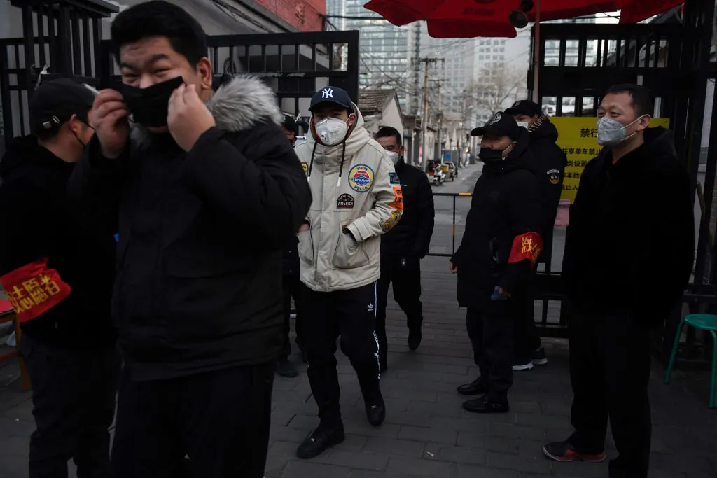 Residents wear face masks as they walk past volunteers manning a checkpoint at the entrance to an alley in Beijing on Feb. 21, 2020. (Greg Baker/AFP via Getty Images)