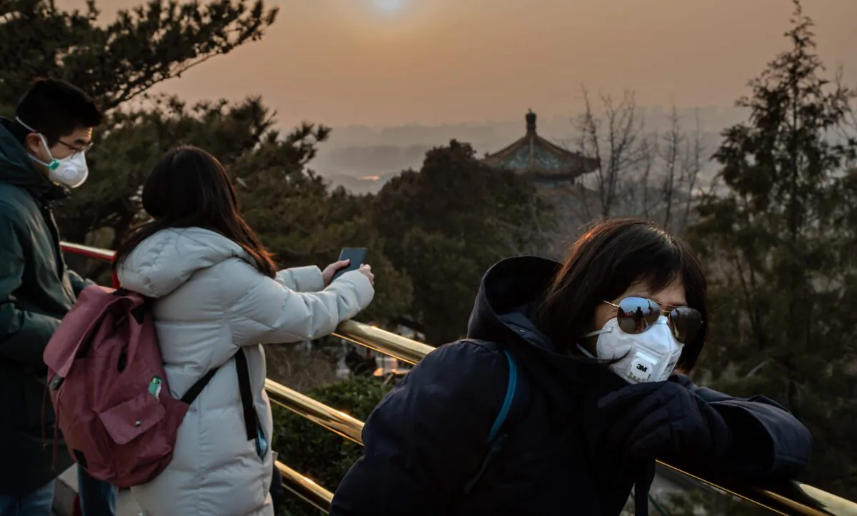 Tourists wearing protective facemasks to help stop the spread of a deadly SARS-like virus which originated in the central city of Wuhan, look at the sunset at Jingshawn park overlooking the Forbidden City in Beijing on Jan. 25, 2020. (NICOLAS ASFOURI/AFP via Getty Images)