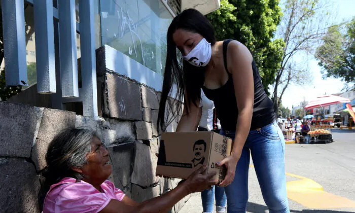 An employee of the clothing brand "El Chapo 701," owned by Alejandrina Gisselle Guzman, daughter of the convicted drug kingpin Joaquin "El Chapo" Guzman, hands out a box with food, face masks and hand sanitizers to an elderly woman as part of a campaign to help cash-strapped elderly people during the COVID-19 disease outbreak, in Guadalajara, Mexico, April 16, 2020.  (Fernando Carranza/Reuters File)