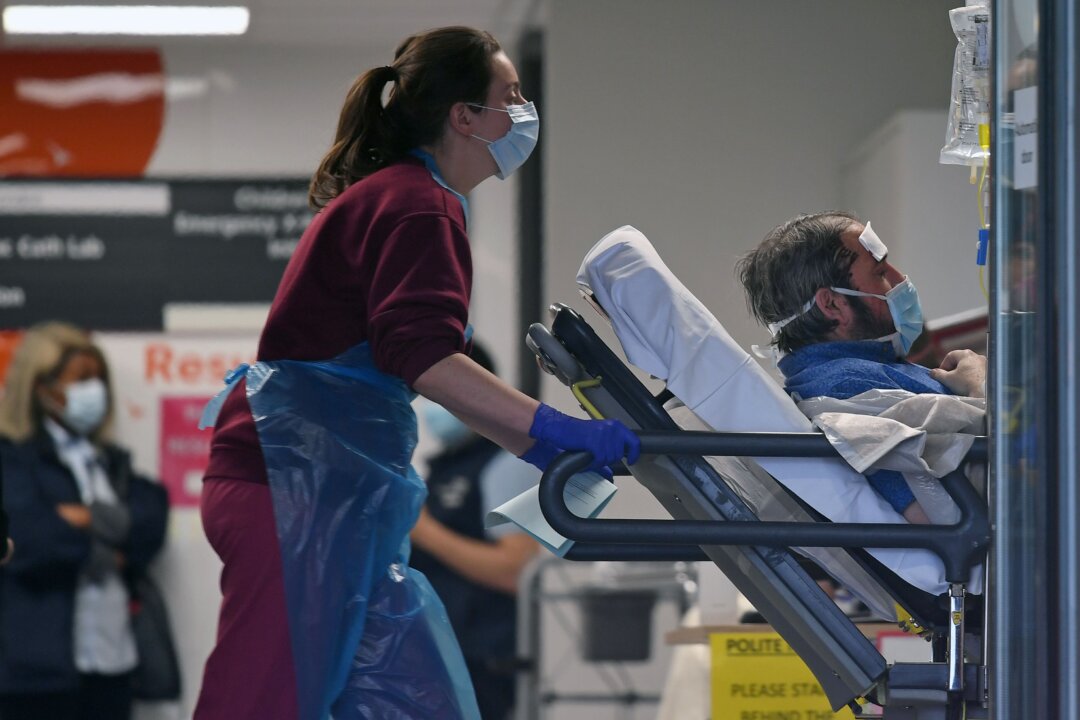 A medical professional in PPE pushes a patient, also wearing a mask, as he lays on a bed, inside St. Thomas's Hospital in north London, on April 1, 2020, (Daniel Leal-Olivas/AFP via Getty Images)