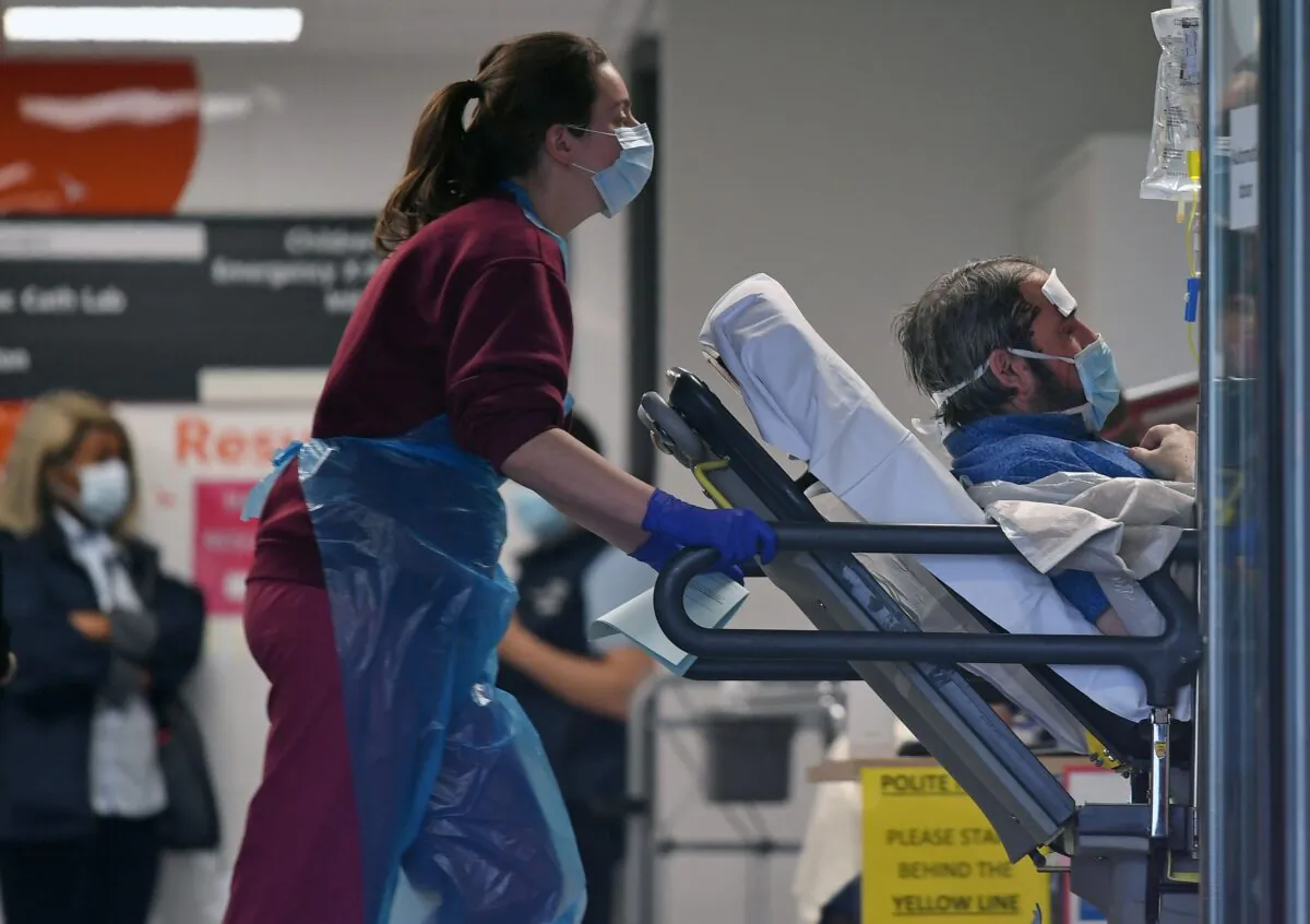 A medical professional in PPE pushes a patient, also wearing a mask, as he lays on a bed inside St. Thomas's Hospital in north London, on April 1, 2020. (Daniel Leal-Olivas/AFP via Getty Images)