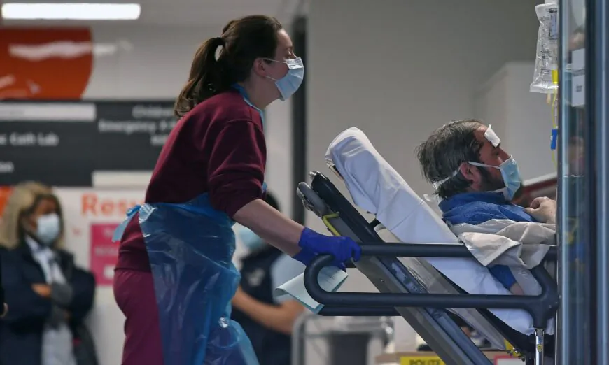 A medical professional in personal protective equipment pushes a patient, also wearing a face mask, as he lays on a bed, at St Thomas' Hospital in north London, on April 1, 2020, (Daniel Leal-Olivas/AFP via Getty Images)