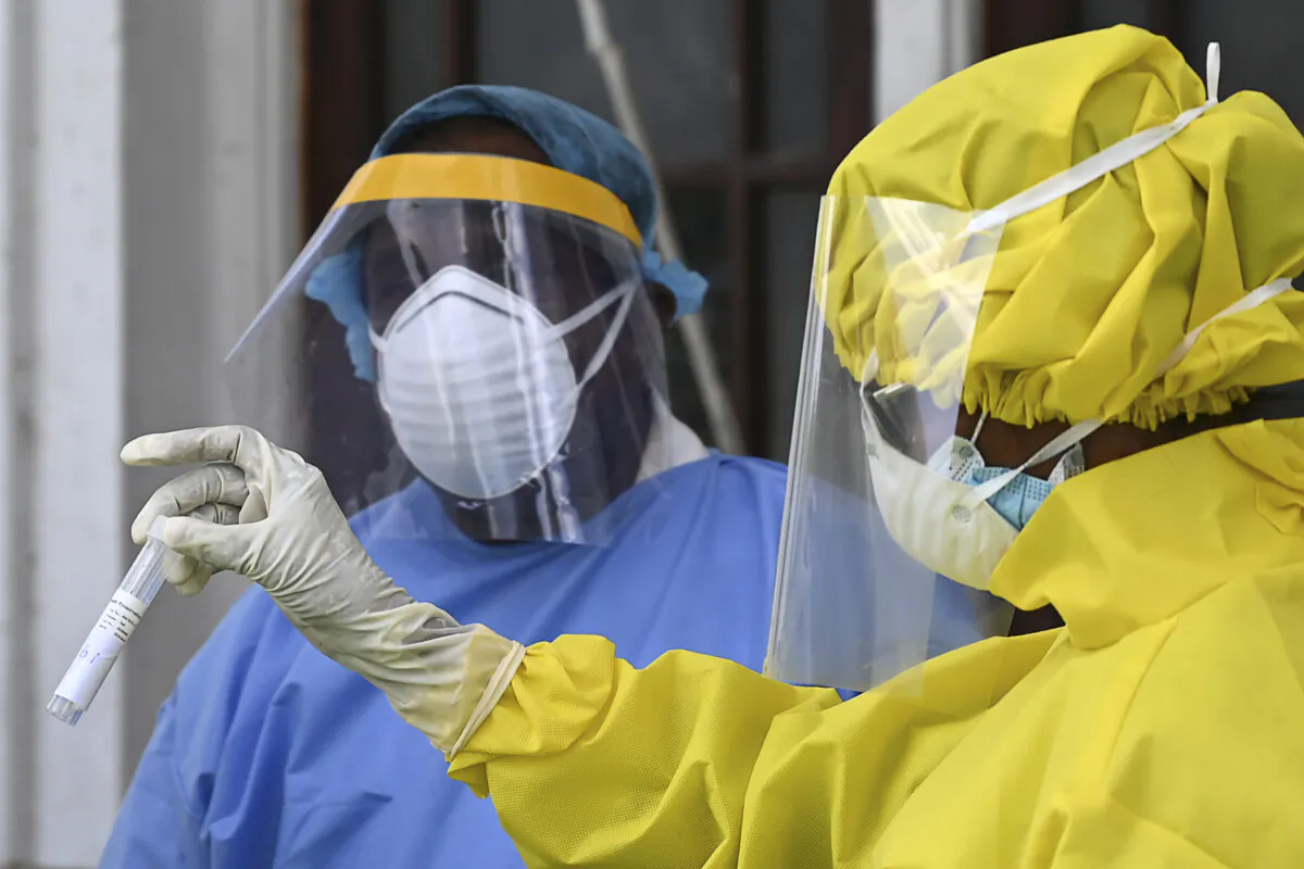 A health worker (R) holds a test tube containing a swab sample for CCP virus testing collected from a man at the Colombo Municipal Council office during a government-imposed nationwide lockdown as a preventive measure against the COVID-19 disease, in Colombo on April 19, 2020. (Ishara S. Kodikara/AFP via Getty Images)