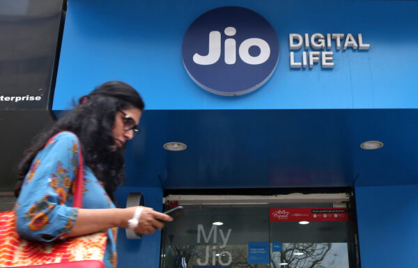 A woman checks her mobile phone as she walks past a mobile store of Reliance Industries' Jio telecoms unit in Mumbai