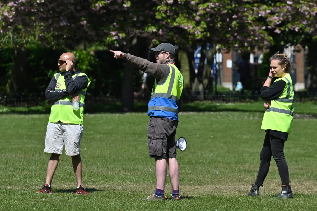 Workers wearing a Tower Hamlets Borough Council hi-vis jackets gesture as they stand in Victoria Park, east London on April 25, 2020, during the national lockdown due to the COVID-19 pandemic. (Justin Tallis/AFP via Getty Images)