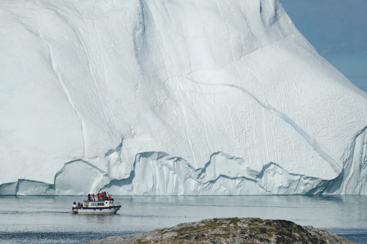 A boat carrying tourists motors past an iceberg at the mouth of the Ilulissat Icefjord during unseasonably warm weather near Ilulissat, Greenland on July 30, 2019. (Sean Gallup/Getty Images)