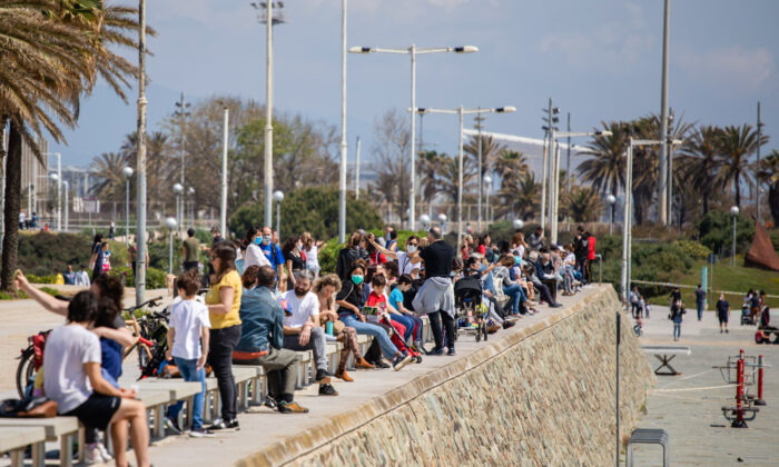 Families with their children sit in a boulevard as police patrol the beach, where access is prohibited, in Barcelona, Spain on April 26, 2020. (Emilio Morenatti/AP)