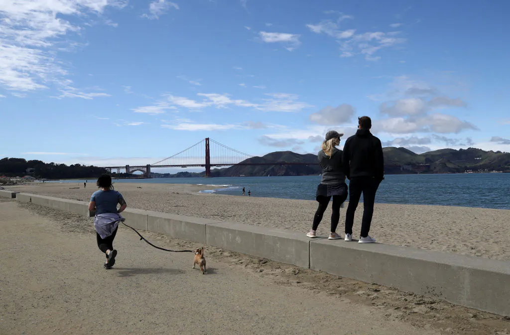 A runner passes people at Crissy Field Beach in San Francisco on March 30, 2020. (Photo by Justin Sullivan/Getty Images)