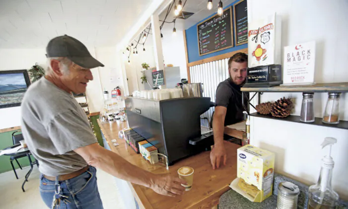 Jonathan Archibald, owner of Mt Taylor coffee, right sells a cup of coffee to Paul Jackson of grants in Grants, N.M. on April 27, 2020. Grants Mayor Martin Hicks in New Mexico opened the city's businesses back up with an executive order, defying the Governor's orders. (Luis Sánchez Saturno/Santa Fe New Mexican via AP)