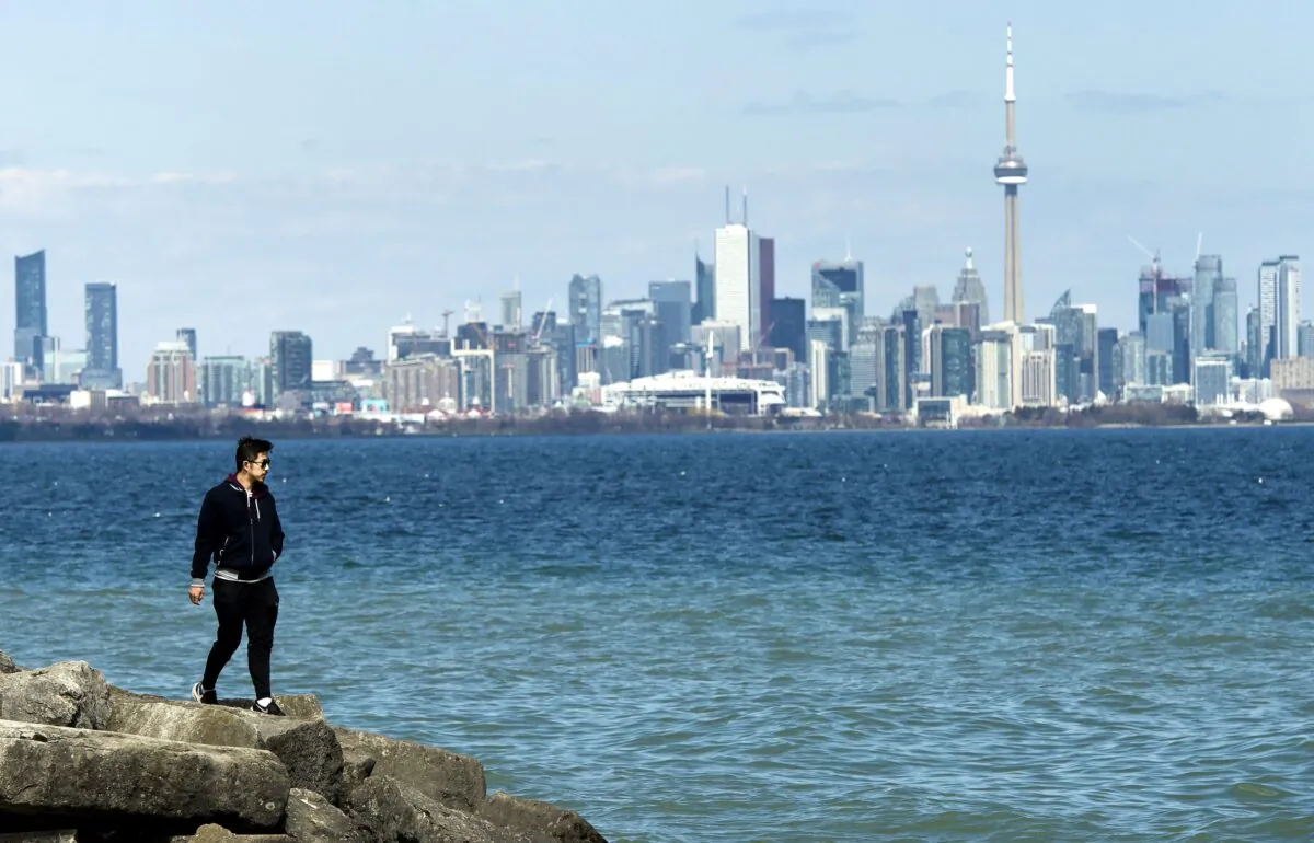 A man walks on the shore of Lake Ontario with the Toronto skyline in the background on April 27, 2020. Provincial governments are beginning to announce plans to progressively reopen businesses and the economy. (The Canadian Press/Nathan Denette)