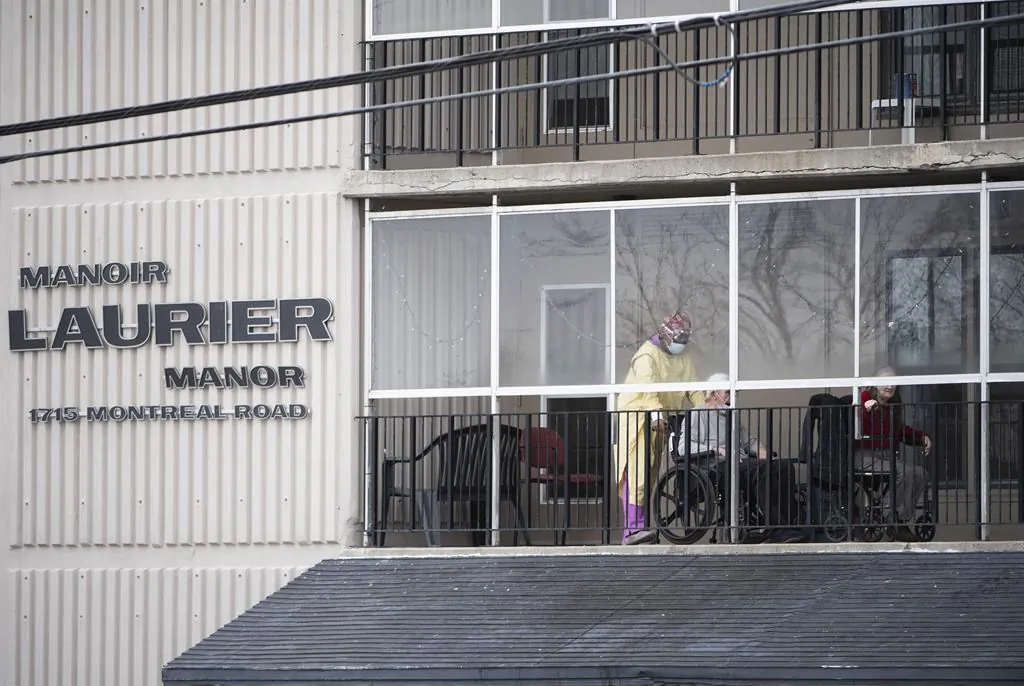 A health care worker wearing personal protective equipment (PPE) works with a resident on a balcony at the Laurier Manor in Ottawa, a long term care facility experiencing an outbreak of COVID-19, on Sunday, April 26, 2020. Ottawa's Mayor Jim Watson says he's ordered the people who run the city's nursing homes to find a way to let family members visit residents through windows again. (Justin Tang/The Canadian Press) 