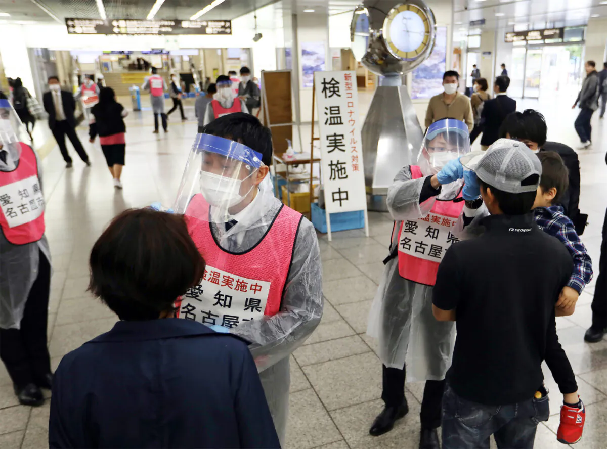 Staff members of Aichi Prefecture, wearing protective gear as a preventive measure to curb the spread of the CCP virus, check the body temperature of passengers arriving at Nagoya railway station, Japan, on April 29, 2020. (STR /Jiji Press/ AFP via Getty Images)