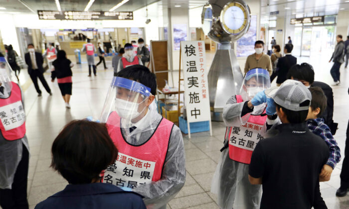 Staff members of Aichi Prefecture, wearing protective gear as a preventive measure to curb the spread of the CCP virus, check the body temperature of passengers arriving at Nagoya railway station, Japan, on April 29, 2020. (STR /Jiji Press/ AFP via Getty Images)