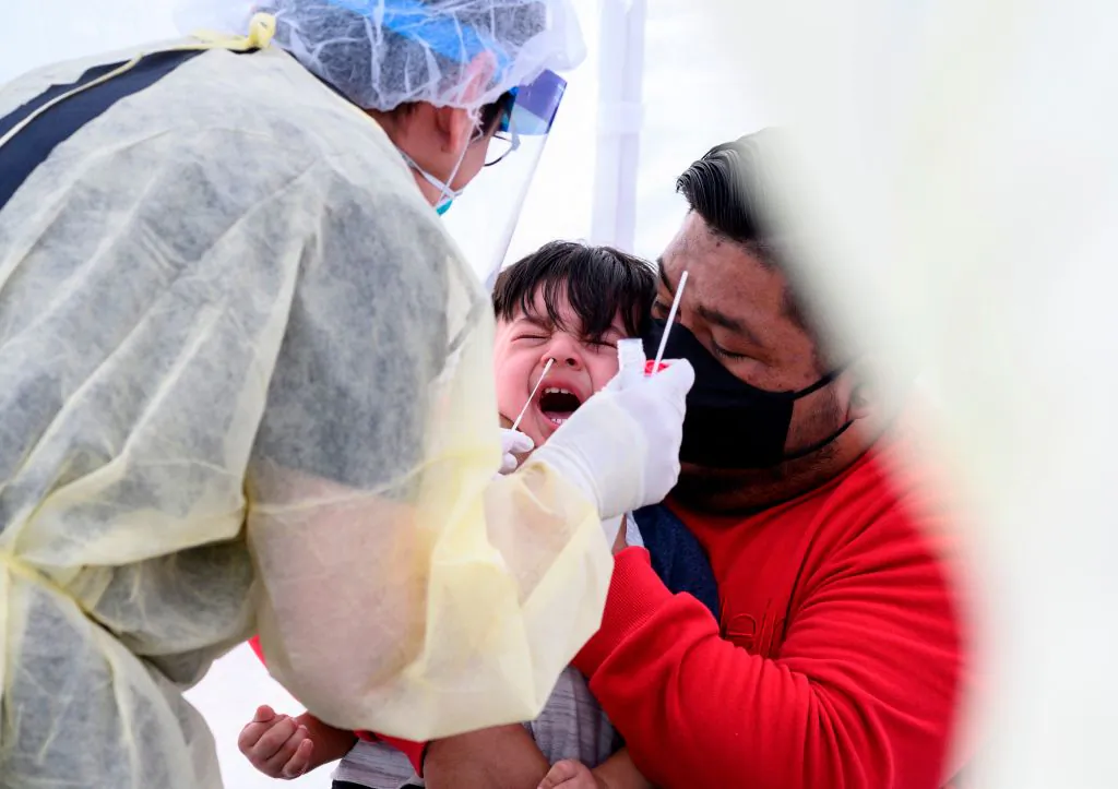 Jose Vatres (R) holds his son Aidin, who reacts as nurse practitioner Alexander Panis (L) takes a nasal swab sample to test for COVID-19 at a mobile testing station in a public school parking area in Compton, Calif., on April 28, 2020. (Robyn Beck/AFP via Getty Images)