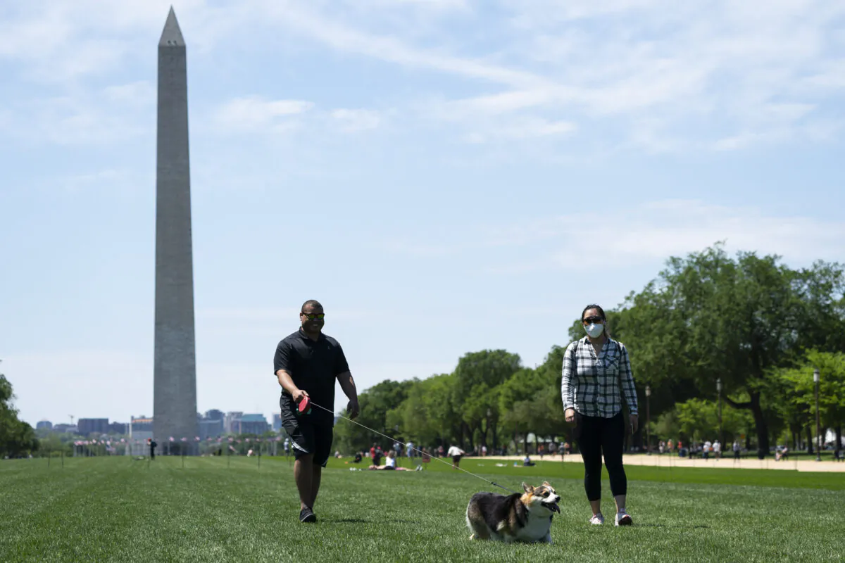 People wear protective masks as they walk a corgi on the National Mall in Washington on May 2, 2020. (Sarah Silbiger/Getty Images)