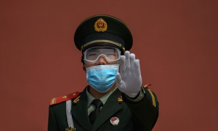 A Chinese paramilitary police officer gestures as he wears a protective mask while standing guard at the entrance to the Forbidden City as it re-opened to limited visitors in Beijing, China, on May 1, 2020. (Kevin Frayer/Getty Images)