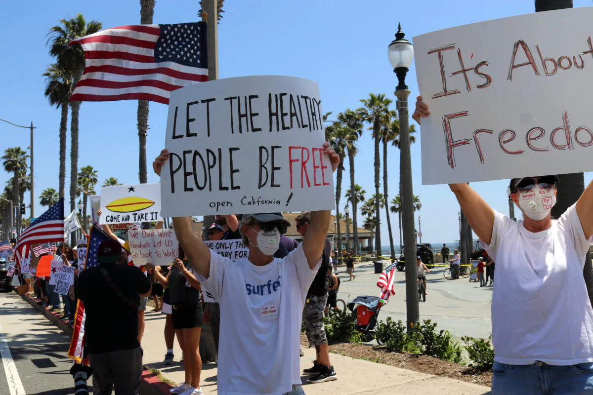 Protesters hold signs in Huntington Beach, Calif., on May 1, 2020. (Jamie Joseph/The Epoch Times)
