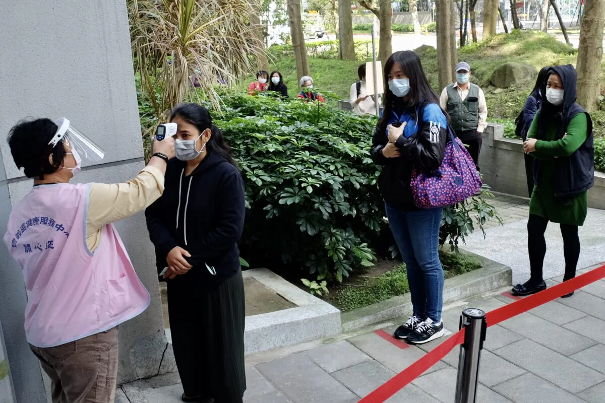 A masked local resident (2nd L) has her temperature checked as people line up to buy face masks from vending machines at the Xinyi District Health Center in Taipei, Taiwan, on April 14, 2020. (Sam Yeh /AFP via Getty Images)