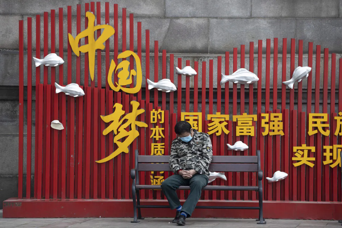 A resident wearing a mask naps on a bench near the government propaganda slogan "Chinese dream" in Wuhan, China, on April 1, 2020. (Ng Han Guan/AP Photo)