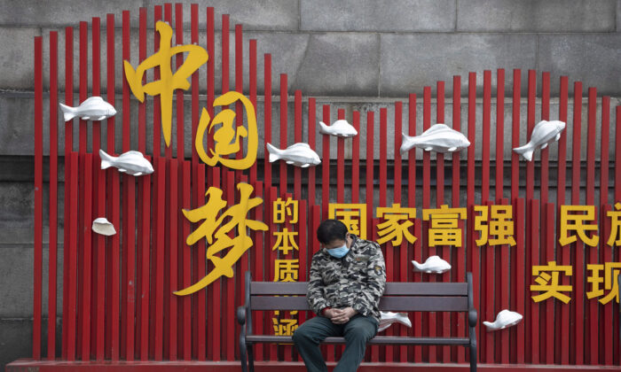 A resident wearing a mask naps on a bench near the Chinese regime's propaganda slogan "Chinese dream" in Wuhan, China, on April 1, 2020. (Ng Han Guan/AP Photo)