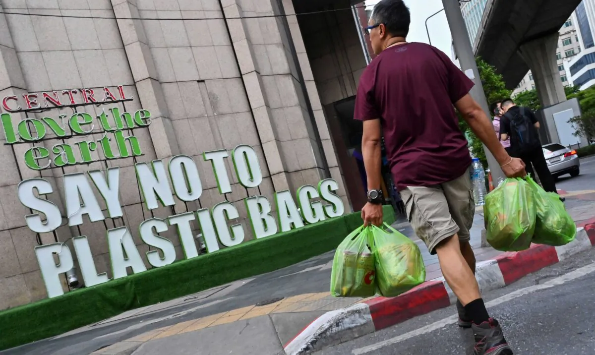 A man carrying goods in plastic bags crosses a street where a sign promoting a plastic bag-free shopping experience is displayed outside a department store in Bangkok on Aug. 13, 2019. (Romeo Gacad/AFP via Getty Images)
