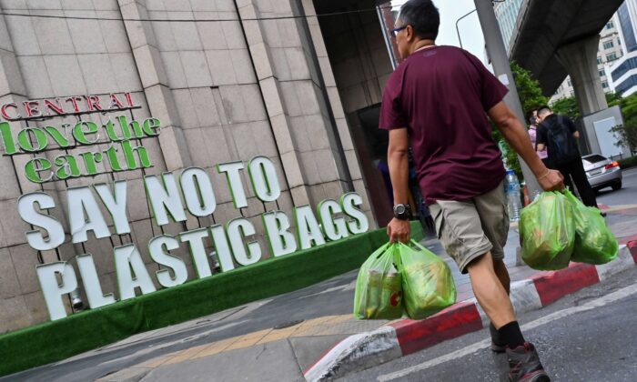 A man carrying goods in plastic bags crosses a street where a sign promoting a plastic bag-free shopping experience is displayed outside a department store in Bangkok on Aug. 13, 2019. (Romeo Gacad/AFP via Getty Images)