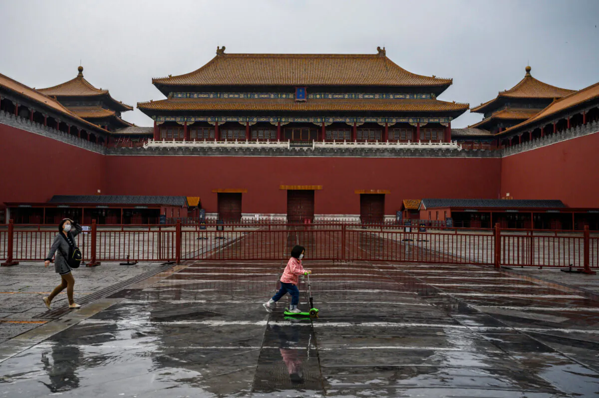 A Chinese girl wears a protective mask as she rides her scooter outside the gate of the Forbidden City, which remains closed to visitors, in Beijing, China, on April 19, 2020. (Kevin Frayer/Getty Images)