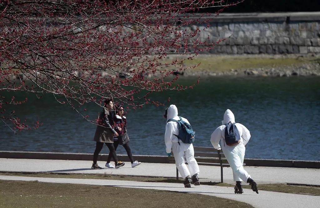 Two people wearing personal protective equipment, including respirators and coverall suits in-line skate on the seawall at Stanley Park in Vancouver, on April 5, 2020. (The Canadian Press/Darryl Dyck)