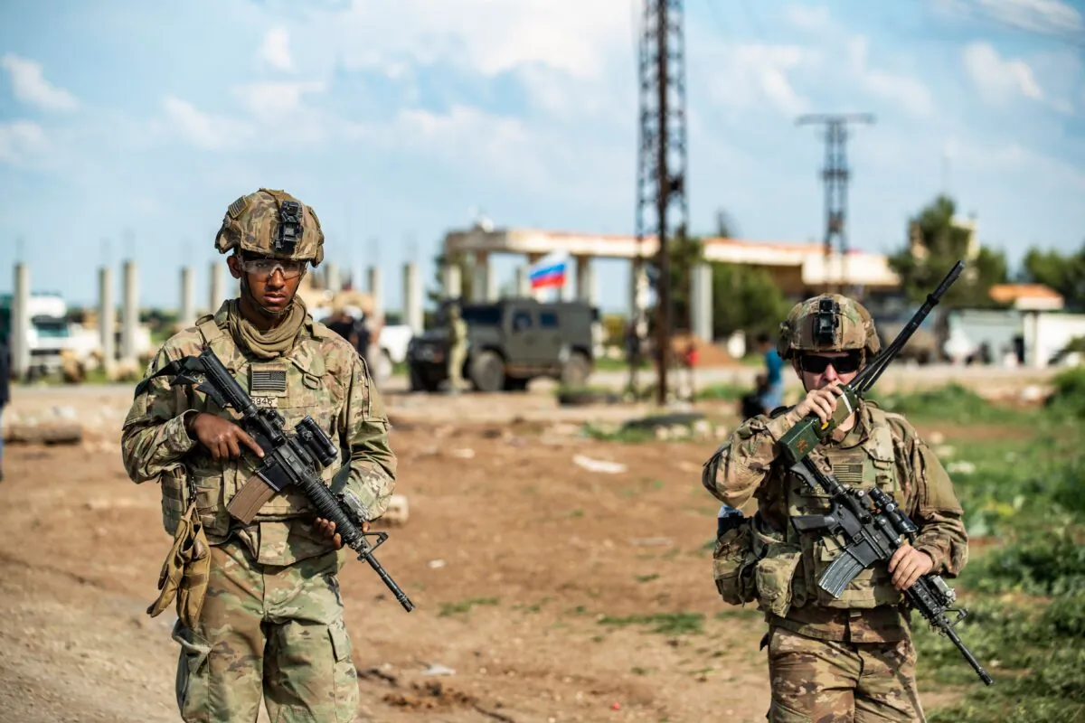 A U.S. soldier uses a handheld radio transceiver while standing alongside another near the village of Tannuriyah in the countryside east of Qamishli in Syria's northeastern Hasakah province on May 2, 2020. (Delil Souleiman/AFP/Getty Images)