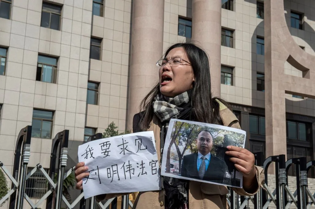 Xu Yan, wife of human rights lawyer Yu Wensheng, holds a piece of paper the reads "I want to request a meeting with Judge Liu Mingwei" and a picture of her husband outside the Xuzhou Intermediate Peoples Court in Xuzhou, China, on Oct. 31, 2019. (Nicolas Asfouri/AFP via Getty Images)