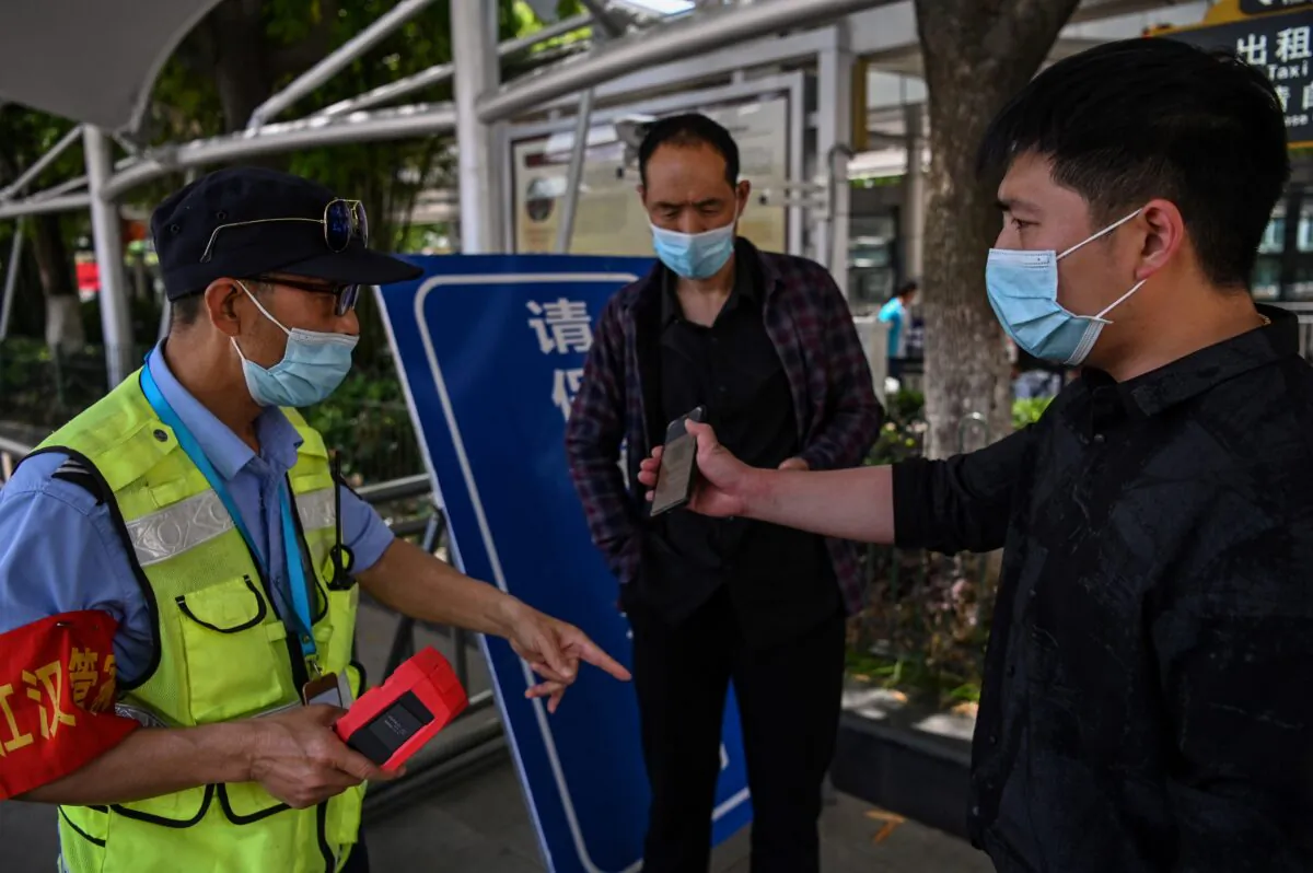 A worker scans a passenger’s cell-phone app generated health code as well as screens his body temperature before the passenger can take a taxi at Hankou railway station in Wuhan, China on May 12, 2020. (HECTOR RETAMAL/AFP via Getty Images)