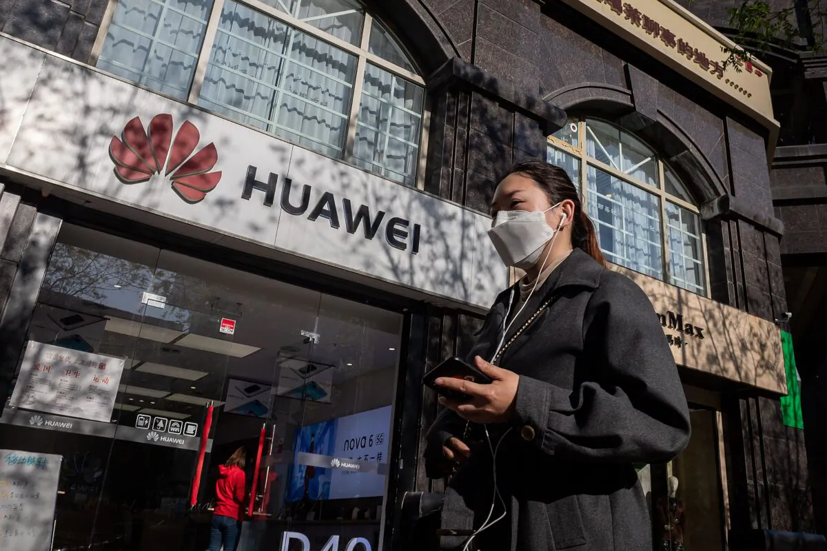 A woman wearing a face mask amid concerns over the COVID-19 coronavirus walks holding her smartphone past a Huawei shop (L) on a street in Beijing on April 22, 2020. (NICOLAS ASFOURI/AFP via Getty Images)