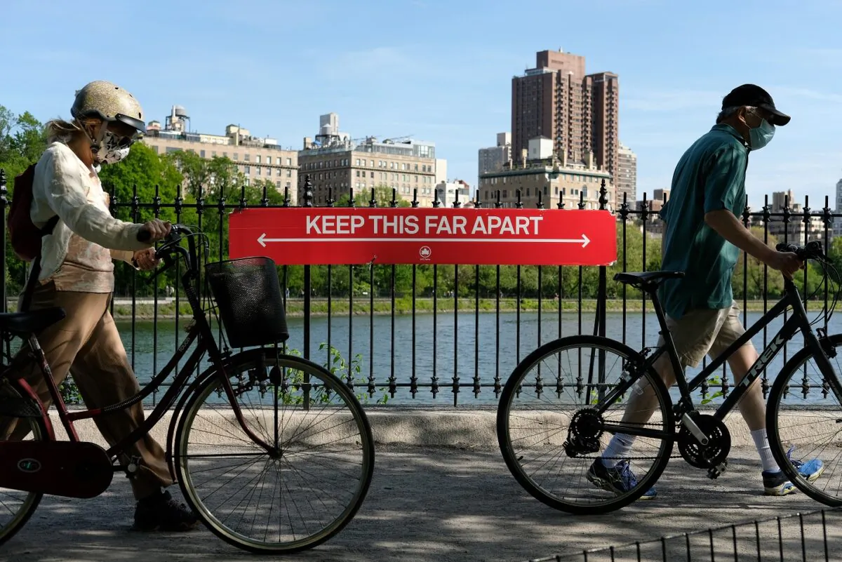 People wearing protective masks walk their bicycles past a social distancing sign reading "Keep This Far Apart" at Jacqueline Kennedy Onassis Reservoir in Central Park in New York City on May 17, 2020. (Dia Dipasupil/Getty Images)