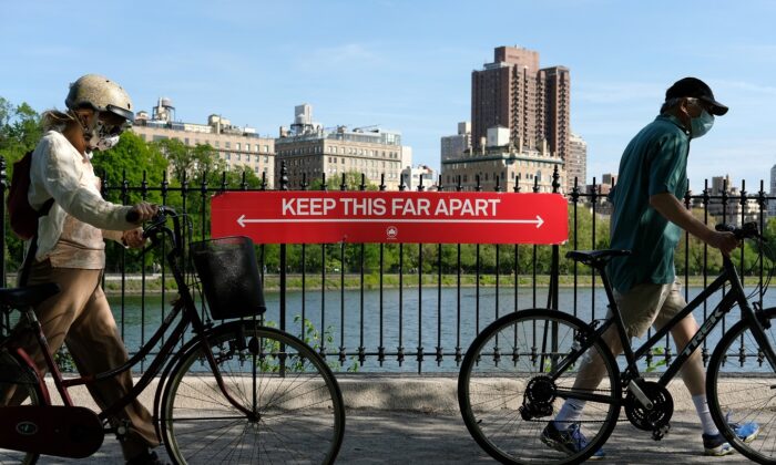 People wearing protective masks walk their bicycles past a social distancing sign reading "Keep This Far Apart" at Jacqueline Kennedy Onassis Reservoir in Central Park in New York City on May 17, 2020. (Dia Dipasupil/Getty Images)