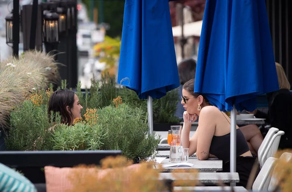 Two women have drinks on the patio at an Earls restaurant, in Vancouver, on May 19, 2020. British Columbia began phase two of the reopening of its economy Tuesday, allowing certain businesses that were ordered closed due to COVID-19 to open their doors to customers if new health and safety regulations are followed. (Darryl Dyck/The Canadian Press)
