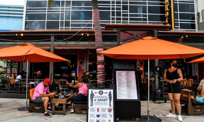 A sign board with precautions is kept in front of a restaurant as people eat sitting outside on Fort Lauderdale Beach Boulevard in Fort Lauderdale, Fla., on May 18, 2020. (Chandan Khanna/AFP via Getty Images)